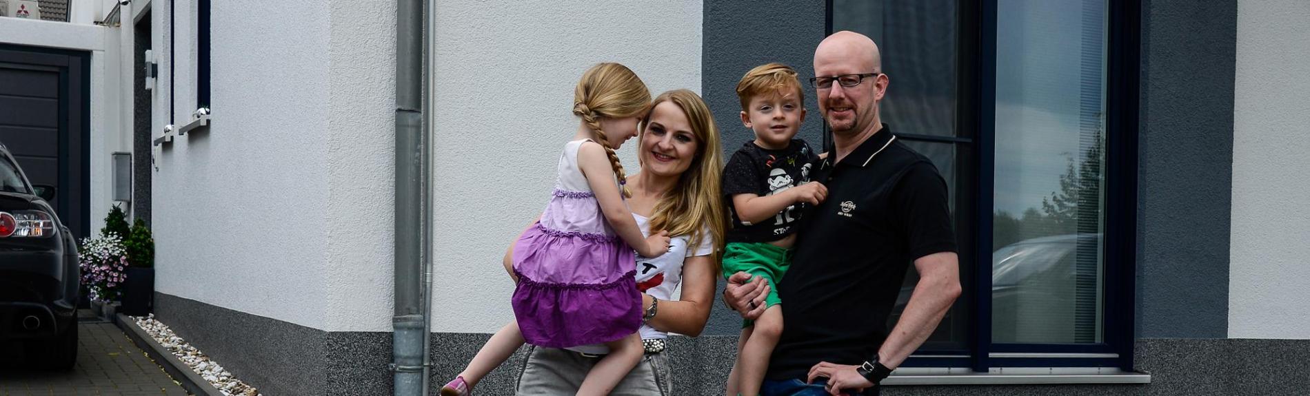 zufriedene Energiespeicher Kunden, vierköpfige Familie vor Ihrem Haus 