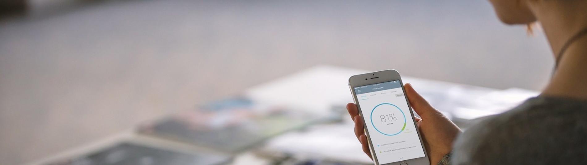 Frau benutzt sonnen App auf ihrem Handy um ihren Strom Verbrauch  zu ermitteln und somit Geld zu sparen 