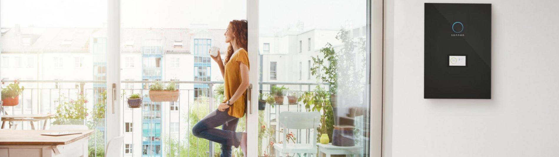 Frau am Fenster macht sich unabhängig mit einem Energiespeicher sonnenBatterie und senkt somit ihre Kosten 