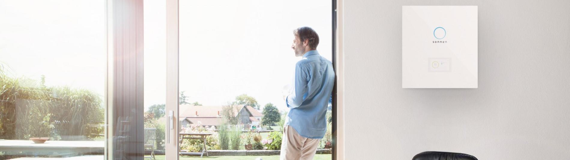 Mann am Fenster in seiner Wohnung macht sich unabhängig mit Solarstromspeicher sonnenBatterie 