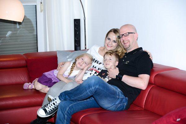 Mutter Vater und zwei Kinder auf der roten Couch, glückliche Stromspeicher Kunden